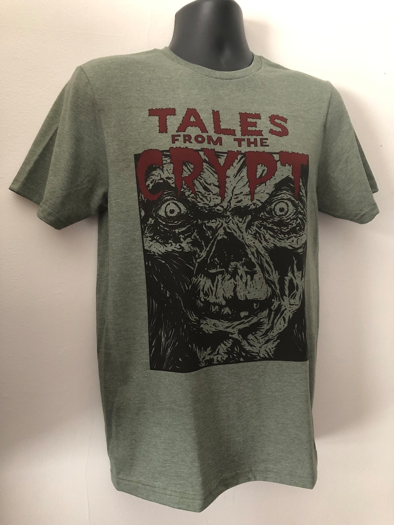 May include: Green t-shirt with a black and white illustration of a monster's face and the text "Tales from the Crypt" in red.