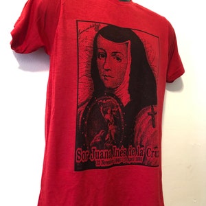 May include: Red t-shirt with a black and white image of Sor Juana In&eacute;s de la Cruz, a Mexican poet and nun. The image includes her name and dates of birth and death: 12 November 1648 - 17 April 1695.