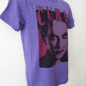May include: Purple t-shirt with a graphic of a man's face and the text "THE CURE" in red.