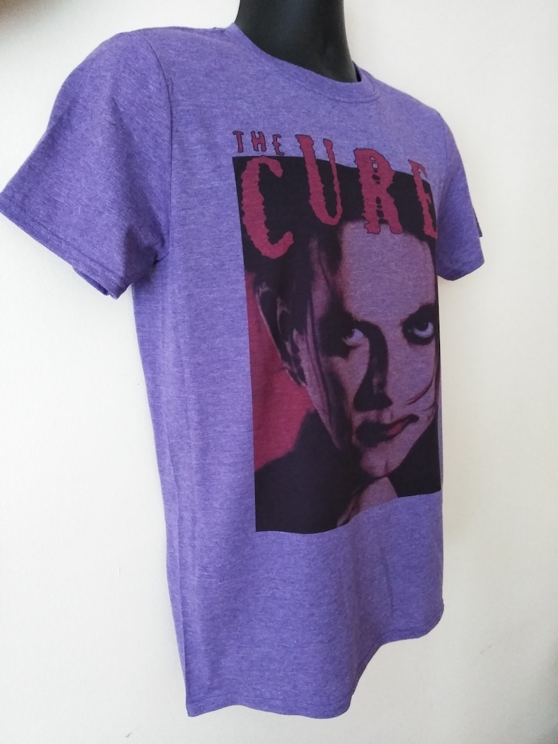 May include: Purple t-shirt with a graphic of a man's face and the text "THE CURE" in red.