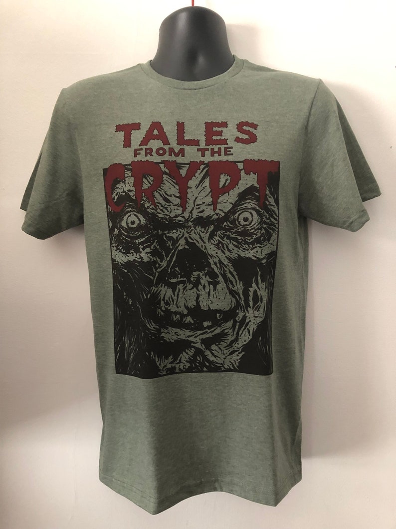May include: Green t-shirt with a black and white illustration of a monster's face and the text "Tales from the Crypt" in red.