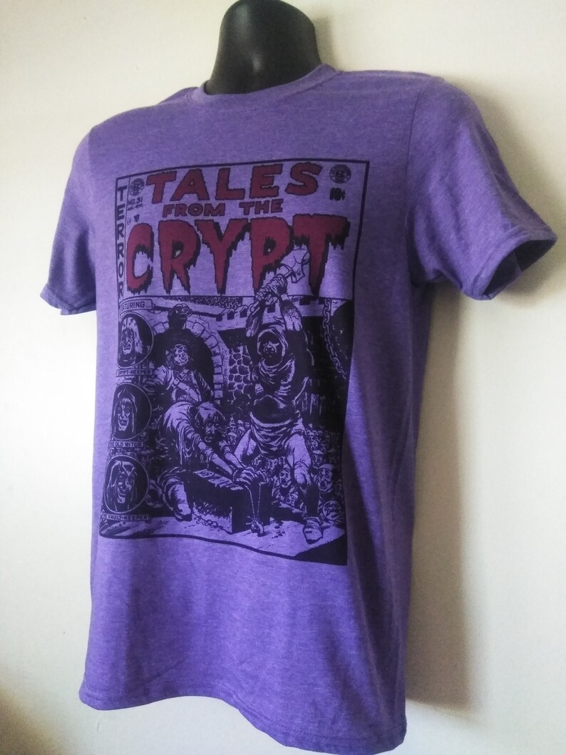 May include: Purple t-shirt featuring a graphic print of a comic book cover with the text "Tales from the Crypt" and a black and white illustration of a scene from the comic book.