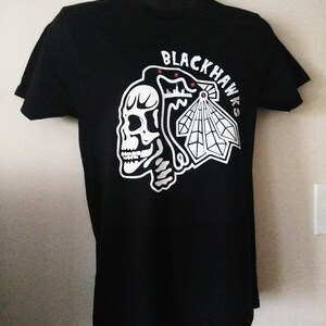 May include: Black t-shirt with a white graphic of a skull and the words "Blackhawks" on the front.