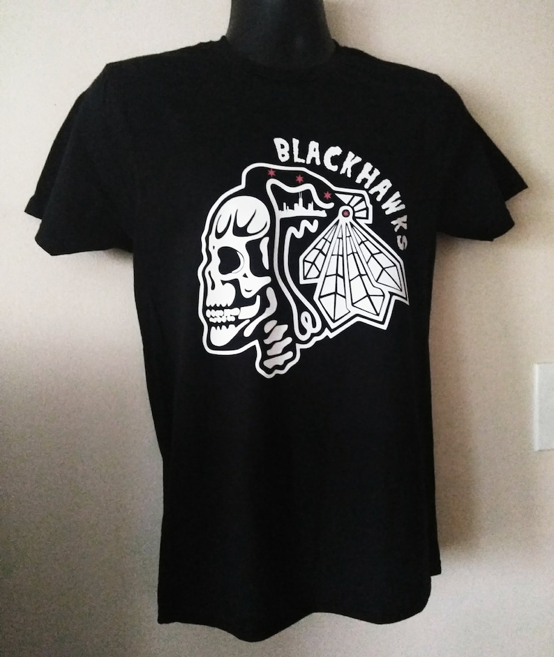 May include: Black t-shirt with a white graphic of a skull and the words "Blackhawks" on the front.