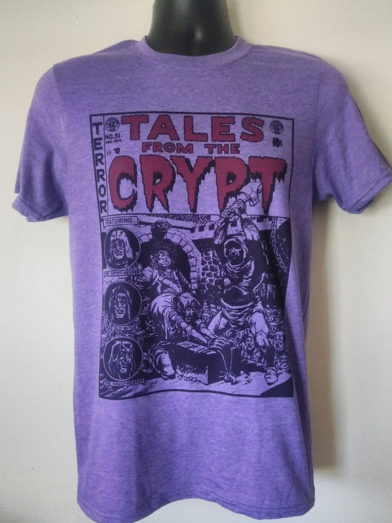 May include: Purple t-shirt featuring a vintage comic book design with the text "Tales From The Crypt" and a black and white illustration of a scene from the comic book.