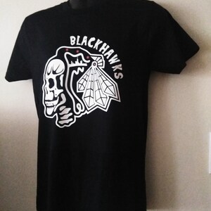 May include: Black t-shirt with a white graphic of a skull and a stylized Native American headdress with the text "BLACKHAWKS" around it.