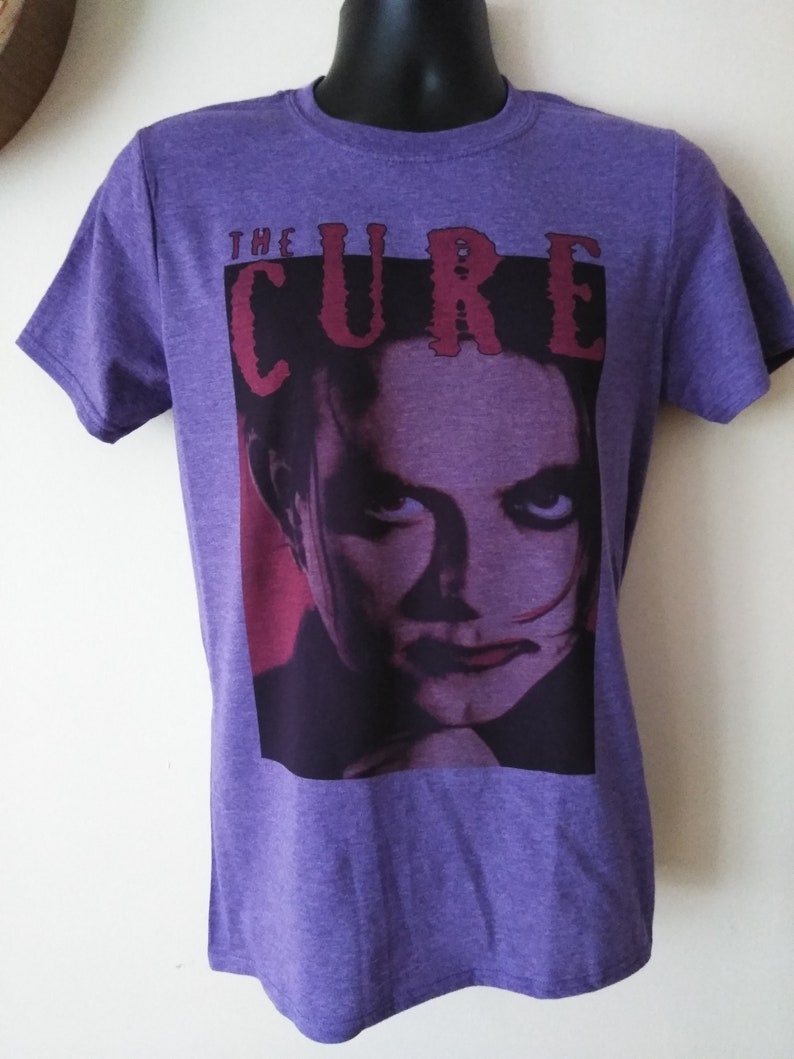 May include: Purple t-shirt with a graphic print of a person's face and the text "THE CURE" in red.