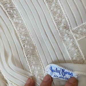 May include: White sheer fabric with a lace trim and a blue label that reads "Judy Bond All Nylon".