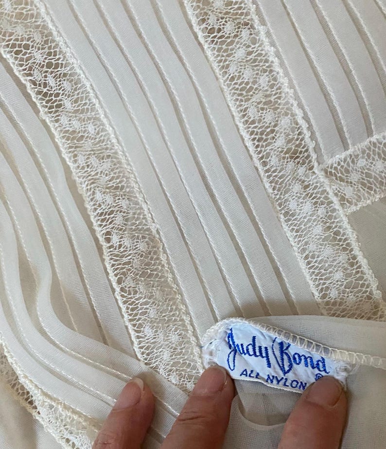 May include: White sheer fabric with a lace trim and a blue label that reads "Judy Bond All Nylon".