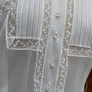 May include: White sheer blouse with a high collar and lace trim. The blouse has a button-up front and is made of a delicate fabric.