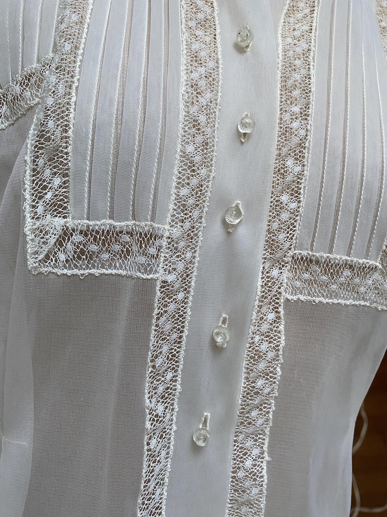 May include: White sheer blouse with a high collar and lace trim. The blouse has a button-up front and is made of a delicate fabric.