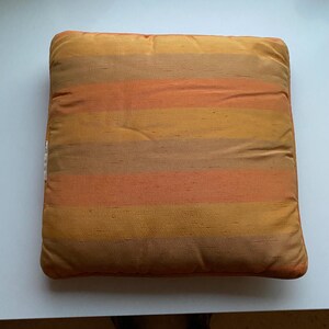 May include: A square throw pillow with a striped pattern in shades of orange, brown, and yellow.