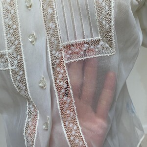 May include: White sheer blouse with a lace trim and button closures. The lace trim features a small polka dot pattern.