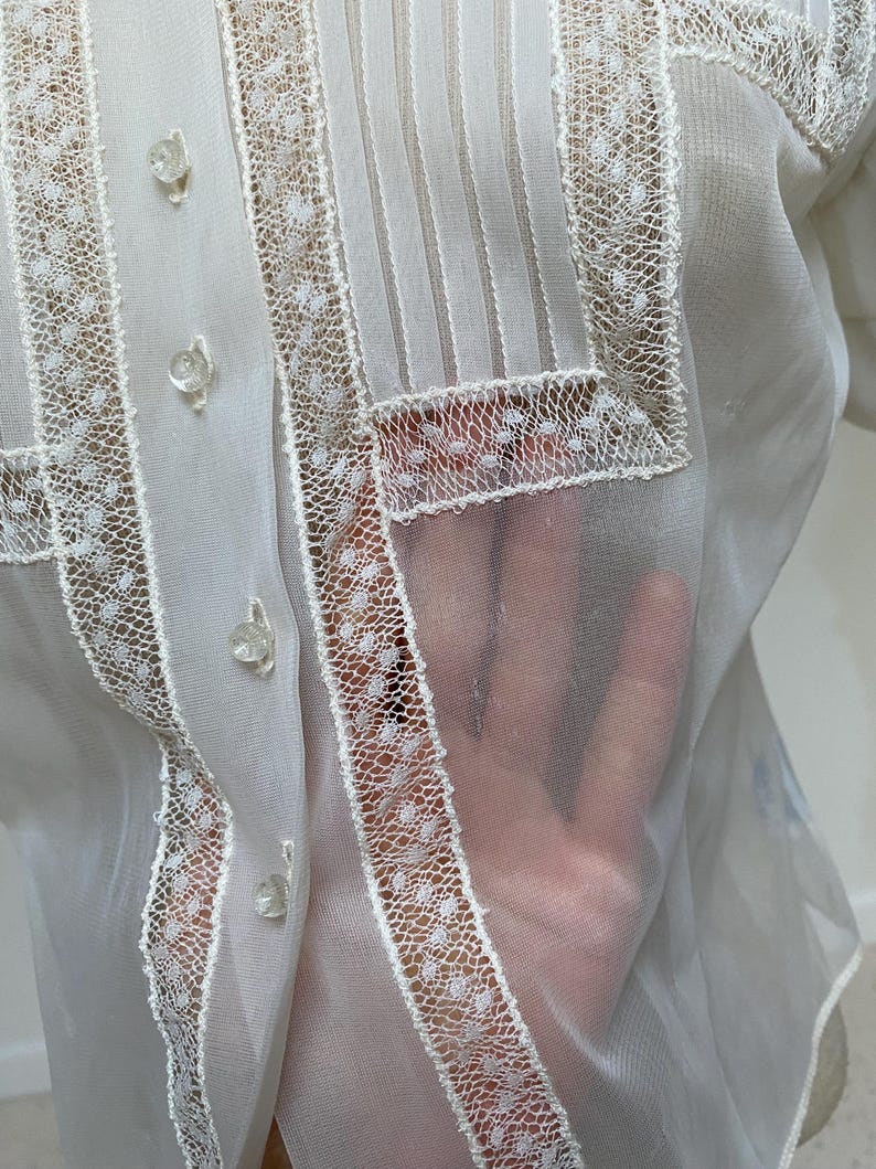 May include: White sheer blouse with a lace trim and button closures. The lace trim features a small polka dot pattern.