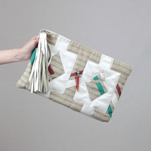 May include: A beige clutch bag with a white leather tassel and geometric design featuring white, beige, red, and green accents.