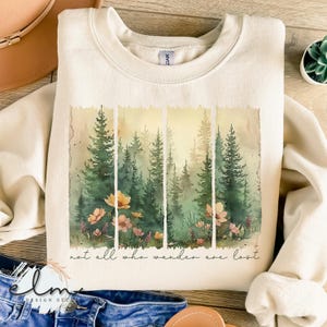 May include: A cream-colored sweatshirt with a watercolor design of a forest with flowers and the text "not all who wander are lost".