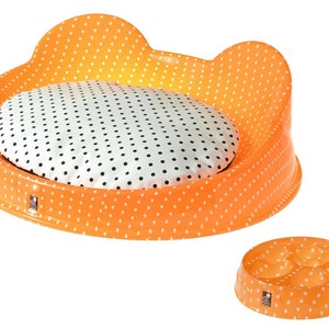 Puede incluir: Cama para mascotas naranja y blanca con un coj&iacute;n redondo extra&iacute;ble. La cama tiene un patr&oacute;n de lunares. Tambi&eacute;n hay un cuenco a juego naranja y blanco con cuatro compartimentos.