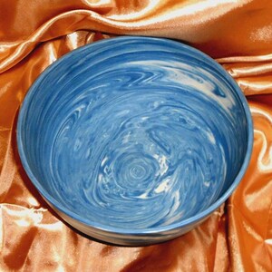 May include: A ceramic bowl with a blue and white marbled design. The bowl has a wide, shallow shape and a smooth, glossy finish. The interior design resembles a galaxy or ocean waves. The bowl is likely handmade.