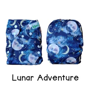 May include: A pair of reusable cloth diapers with a blue and white moon and star print. The print includes the text "Kijani". The diapers are labeled "Lunar Adventure".