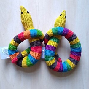 May include: Two crocheted rainbow snake toys. The snakes are made of yellow, red, orange, yellow, green, blue, purple, and brown yarn. The snakes are curled into a circle shape.