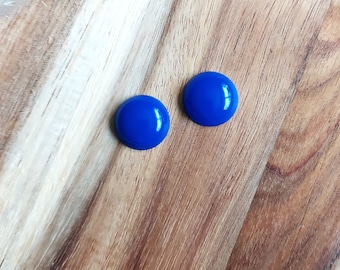 May include: A pair of blue round stud earrings. The earrings are on a wooden surface.
