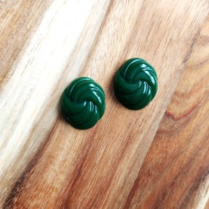 May include: Two dark green swirl-shaped earrings on a wooden surface.