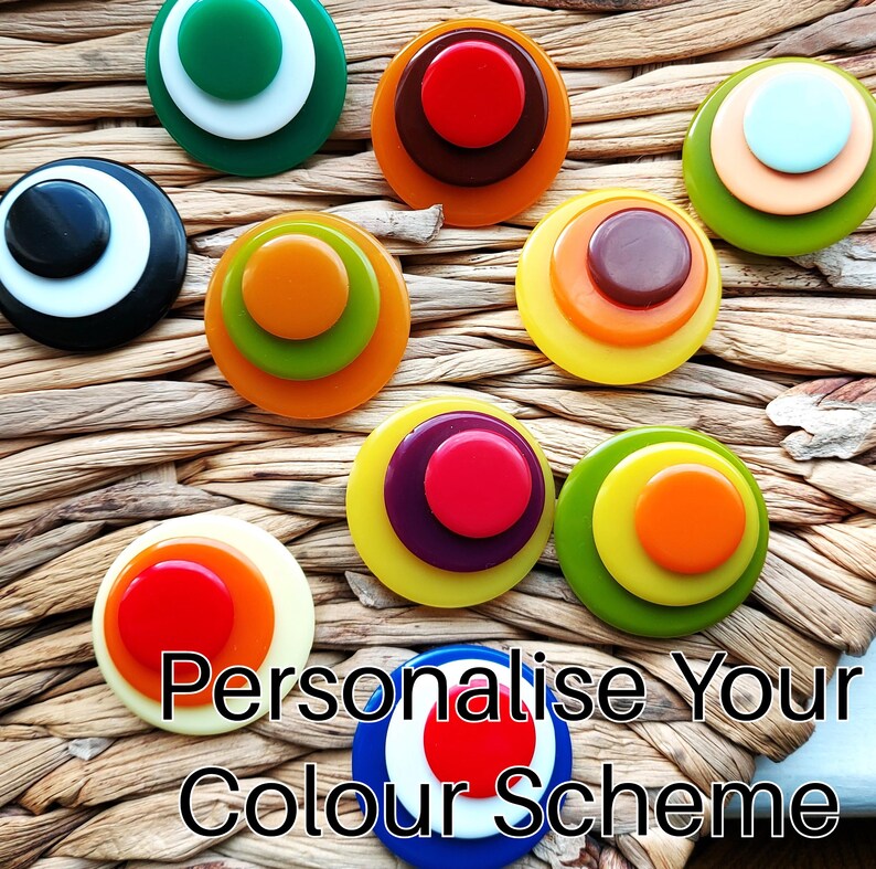 K&ouml;nnte beinhalten: Eine Sammlung kreisf&ouml;rmiger, mehrschichtiger Kn&ouml;pfe in verschiedenen Farbkombinationen, darunter Rot, Orange, Gelb, Gr&uuml;n, Blau, Wei&szlig; und Schwarz. Der Text "Personalise Your Colour Scheme" ist am unteren Bildrand eingeblendet.