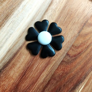 May include: A black flower-shaped button with a white center. The button is made of plastic and has a smooth finish.