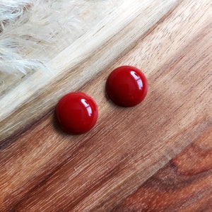 Peut inclure: Deux boucles d'oreilles rondes rouges sur une surface en bois.
