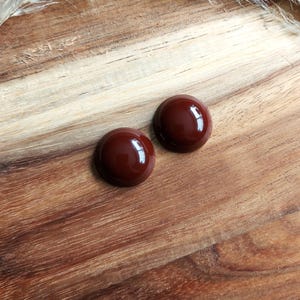 May include: Two round, brown, glossy earrings on a wooden surface.