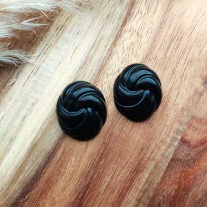 Könnte beinhalten: Ein Paar schwarze, spiralförmige Ohrringe. Die Ohrringe sind aus einem glatten, glänzenden Material.