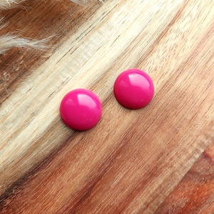 May include: Two bright pink round stud earrings on a wooden surface.