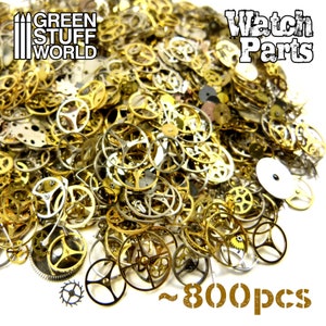 Pode incluir: Um grande monte de peças de relógio sortidas em ouro e prata, incluindo engrenagens, rodas e outros componentes. O monte está sobre um fundo branco e o texto "Watch Parts" e "~800pcs" é visível na imagem.