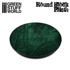 May include: A round, dark green velvet-covered display base with a black edge. The text "GREEN STUFF WORLD" and "Round Block Plinth" are printed on the top of the image. This product is designed for displaying miniatures and models.