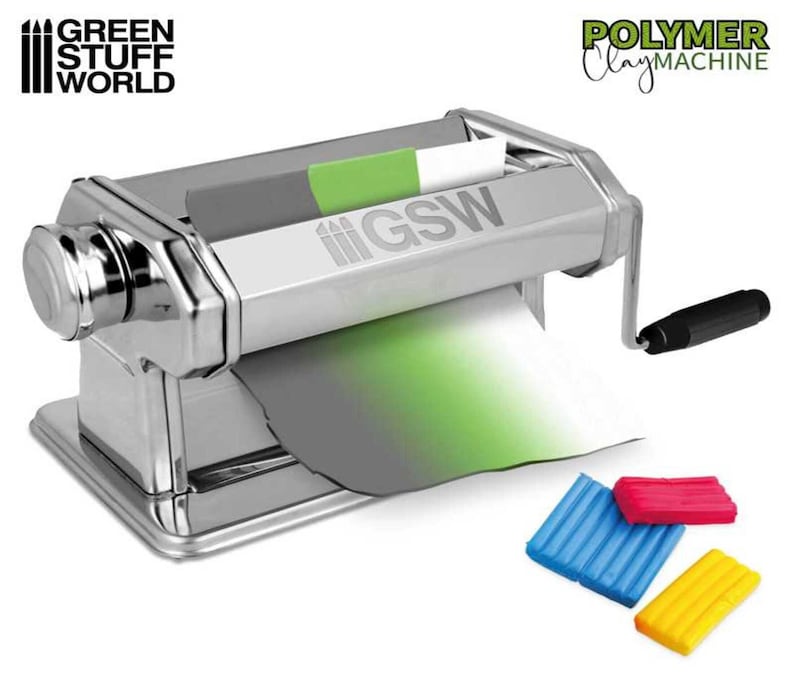 May include: A silver polymer clay machine with a crank handle. The machine has a green, gray, and white sheet of clay going through it. The machine is labeled "Green Stuff World" and "Polymer Clay Machine". There are four small blocks of clay in different colors: blue, red, yellow, and green.