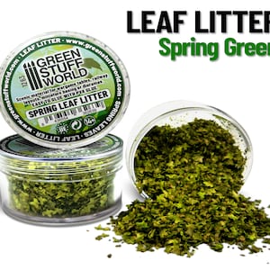 Può includere: Un barattolo di plastica trasparente pieno di lettiera di foglie verdi, etichettato "Spring Leaf Litter" e "Green Stuff World". Il barattolo sta versando la lettiera di foglie su una superficie bianca. L'etichetta dice anche "Spring Green".