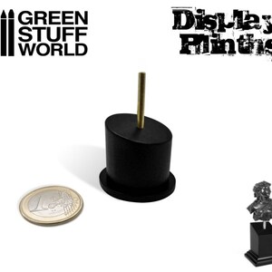 Puede incluir: Soporte de exhibición negro con una varilla de metal dorado. El soporte es aproximadamente del tamaño de una moneda de 1 euro. El soporte está diseñado para sostener pequeñas figuras u otros objetos.