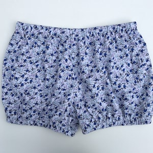 May include: White cotton shorts with a blue floral print. The shorts have an elastic waistband and a gathered hem.