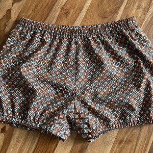 May include: Brown, white and orange patterned shorts with a gathered elastic waistband.
