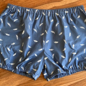 May include: Blue cotton shorts with a white feather print. The shorts have an elastic waistband and a gathered hem.