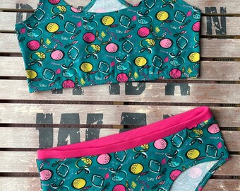 May include: A teal blue and pink two-piece underwear set with a lemon print. The set includes a racerback sports bra and a pair of bikini-style underwear.