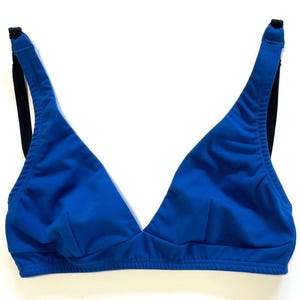Può includere: Un reggiseno blu a forma di triangolo con spalline nere. Il reggiseno è realizzato in un materiale morbido e ha un design a scollo a V. Le spalline sono regolabili.
