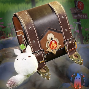 May include: A brown leather satchel with gold accents and a red and gold emblem. A white plush fox with a pink tail is attached to the bag.