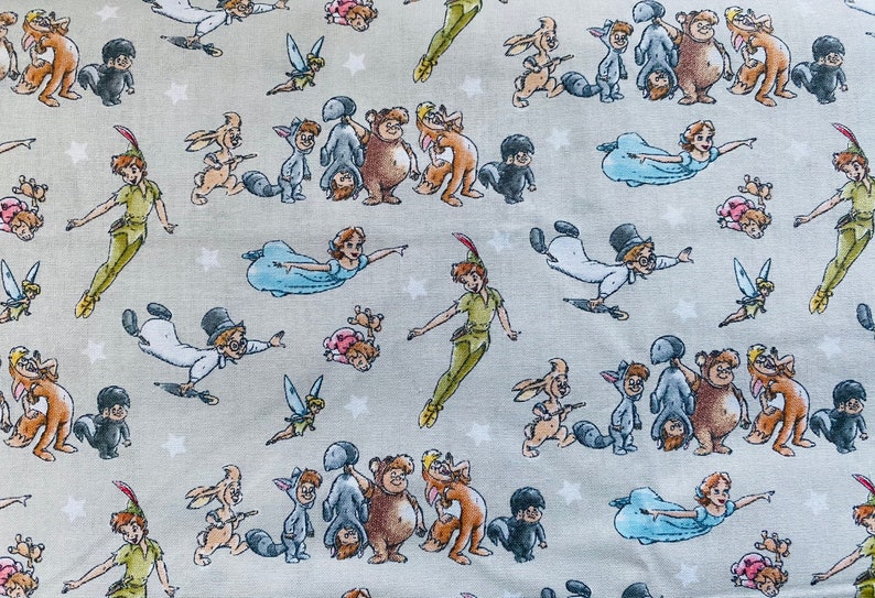 K&ouml;nnte beinhalten: Ein grauer Stoff mit einem sich wiederholenden Muster von Peter Pan und Tinkerbell-Charakteren aus dem Disney-Film Peter Pan. Die Figuren sind in verschiedenen Posen dargestellt, darunter fliegend, stehend und sitzend. Der Stoff ist perfekt f&uuml;r Bastelprojekte wie Quilts, Kissen und Tragetaschen.