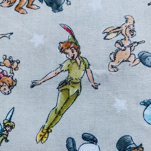 K&ouml;nnte beinhalten: Ein hellgrauer Stoff mit einem sich wiederholenden Muster aus verschiedenen Disney-Charakteren, darunter Peter Pan, Tinkerbell und ein Kaninchen. Die Figuren sind alle im Cartoon-Stil gehalten und fliegen oder stehen auf dem Stoff.