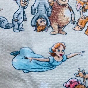 K&ouml;nnte beinhalten: Ein hellblauer Stoff mit wei&szlig;em Hintergrund, auf dem verschiedene Comicfiguren abgebildet sind, darunter eine fliegende Tinkerbell, ein Waschb&auml;r, ein B&auml;r und ein Fuchs. Die Figuren sind alle in einem skurrilen Stil gehalten und in einem zuf&auml;lligen Muster angeordnet.
