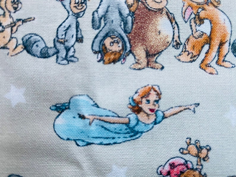 K&ouml;nnte beinhalten: Ein hellblauer Stoff mit wei&szlig;em Hintergrund, auf dem verschiedene Comicfiguren abgebildet sind, darunter eine fliegende Tinkerbell, ein Waschb&auml;r, ein B&auml;r und ein Fuchs. Die Figuren sind alle in einem skurrilen Stil gehalten und in einem zuf&auml;lligen Muster angeordnet.