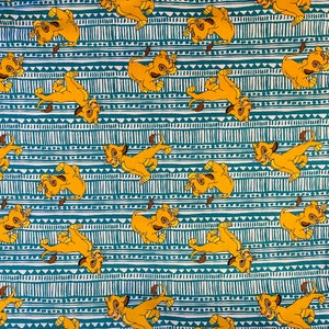 May include: A teal and white fabric with a repeating pattern of yellow lion cubs. The cubs are in various poses, including walking, running, and sitting. The background is a teal and white geometric pattern.