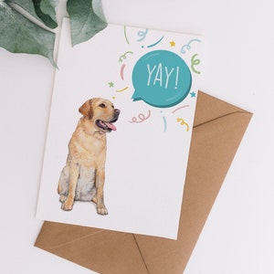 May include: Greeting card featuring a watercolor illustration of a yellow Labrador Retriever with its tongue out. The card has a speech bubble with the word "YAY!" and colorful confetti. Includes a brown envelope.