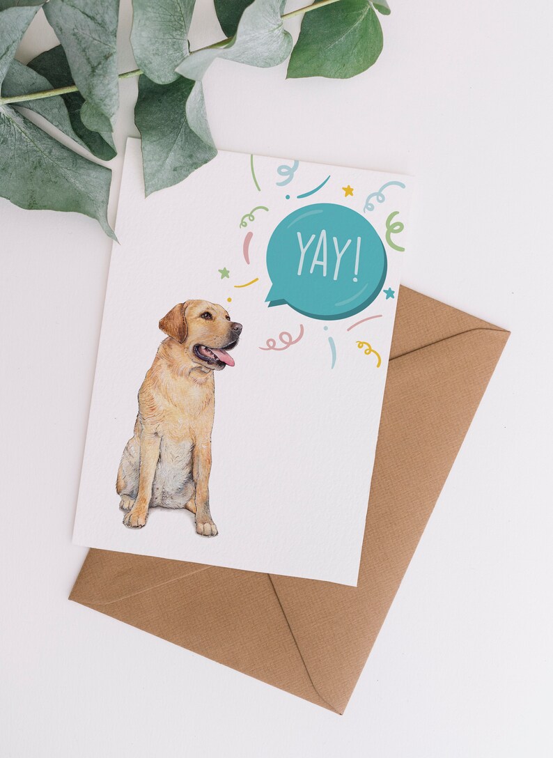 May include: Greeting card featuring a watercolor illustration of a yellow Labrador Retriever with its tongue out. The card has a speech bubble with the word "YAY!" and colorful confetti. Includes a brown envelope.